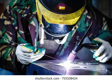 Professional welder in mask welds steel with electric torch tool.Factory worker welding metal parts with burner electrode.Manual labor specialist at metal shop.Bright electric torch burns iron