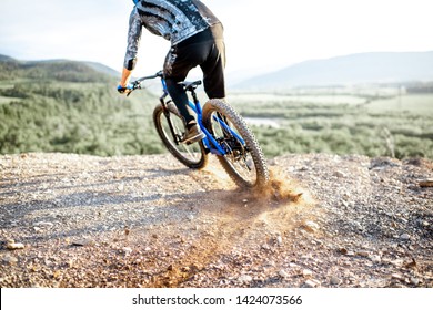 Professional well-equipped cyclist riding extremely on the rocky mountains raising dust behind during the sunset - Shutterstock ID 1424073566