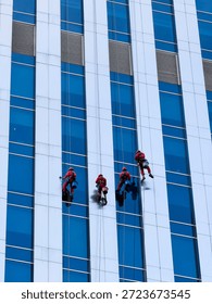 Professional window cleaners are using rope access to clean the exterior of a modern office building. A team of industrial climbers is cleaning the glass facade of a skyscraper, symbolizing maintenanc