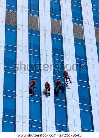 Professional window cleaners are using rope access to clean the exterior of a modern office building. A team of industrial climbers is cleaning the glass facade of a skyscraper, symbolizing maintenanc