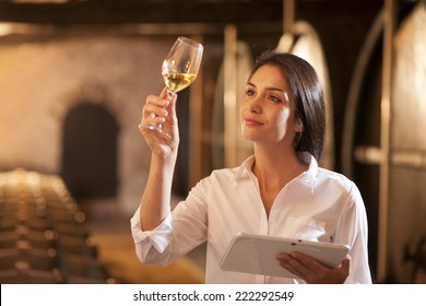 Professional winemaker female tasting a glass of white wine in his traditional cellar surrounded by wooden barrels. She uses a digital tablet - Powered by Shutterstock