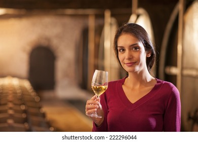 Professional winemaker female tasting a glass of white wine in his traditional cellar surrounded by wooden barrels - Powered by Shutterstock