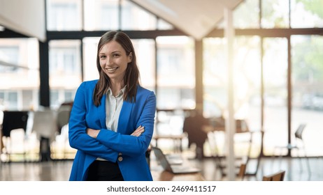 A professional woman with a confident smile stands in a bright, airy office space, dressed in a smart blue blazer with arms crossed.

 - Powered by Shutterstock