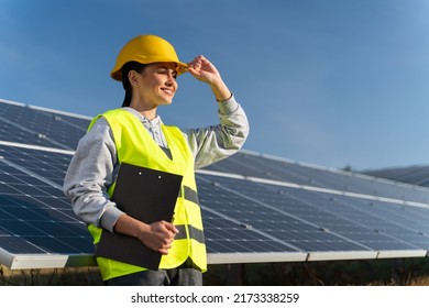 Professional woman engineer looking away with pleasure smile while working at ecological green field with solar panels. Photovoltaic power station concept  - Shutterstock ID 2173338259