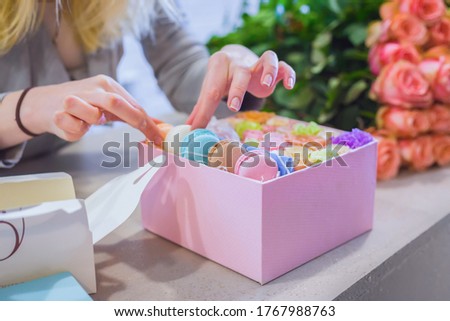 Professional woman floral artist, florist making gift box with flowers and cake macarons at workshop, flower shop. Floristry, biscuit, holiday, wedding, birthday, handmade and small business concept