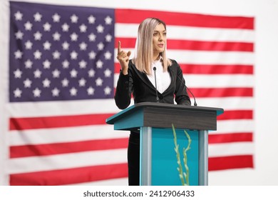 Professional woman giving a speech on a pedestal and gesturing with finger in front of an american flag - Powered by Shutterstock