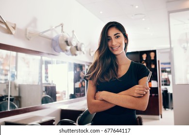 Professional woman hairdresser in salon with scissors in hand. Smiling young woman standing in salon with folded hands.