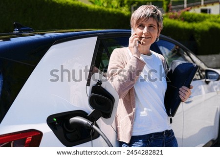 Professional woman on the phone by her EV, blending productivity with sustainability.