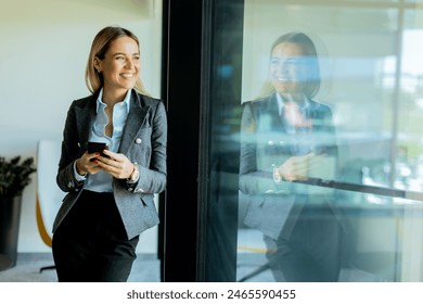 Professional woman smiles while speaking on her phone in a bright, modern office. Sunlight filters through large windows, creating a warm atmosphere - Powered by Shutterstock