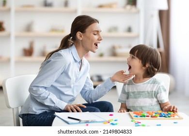 Professional woman speech therapist helping little boy to pronounce right sounds, showing mouth articulation at office, free space - Shutterstock ID 2149804833