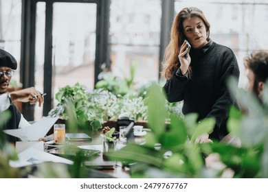 A professional woman is taking a call during a casual business meeting in a plant-filled cafe, highlighting multitasking and collaboration. - Powered by Shutterstock