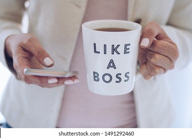 Professional woman using mobile phone and holding a cup that says LIKE A BOSS