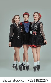 Professional women's Irish dance ensemble in concert costumes and Ghillies Hard Shoes pose together in a row. Full-length studio portrait on a grey background. - Shutterstock ID 2311822277