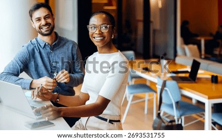 A professional work environment featuring two individuals, one caucasian male and one black female, seated together engaging in productive and focused activities with a laptop.