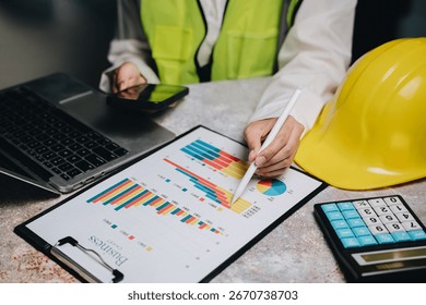 Professional worker analyzes data with graphs and charts using laptop, smartphone, and calculator on desk.