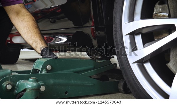 A professional worker in a car service\
raises (lowers) a car on a jack. Concept from: Auto car wash, Car\
Garage, Tools, Maintenance.