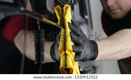 Professional worker guy (Man) wipes the car after painting (ceramics) in a special uniform with black gloves and with a yellow rag. Concept of: Young master, Preparing for the sale, Cleaning.