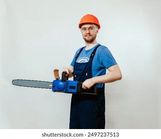 Professional worker holding a chainsaw, wearing a blue shirt, blue overalls, orange hard hat. Perfect for advertising safety gear, promoting construction and forestry services. Man with a chainsaw