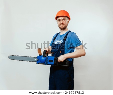 Professional worker holding a chainsaw, wearing a blue shirt, blue overalls, orange hard hat. Perfect for advertising safety gear, promoting construction and forestry services. Man with a chainsaw