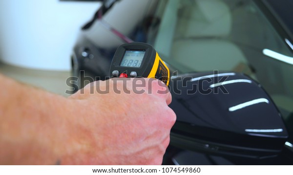 The\
professional worker holds a pistol in his hand measuring the\
temperature of the auto repair shop, car\
washing.