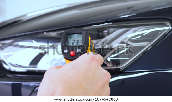 The\
professional worker holds a pistol in his hand measuring the\
temperature of the auto repair shop, car\
washing.