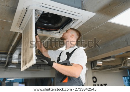Professional worker installing air conditioner filter, providing heating, ventilation, and air conditioning maintenance in office building