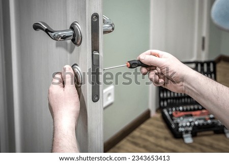 Professional worker installing the part of lock in wooden door by the screwdriver. Industrial theme