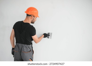 Professional worker plastering wall with putty knife indoors.