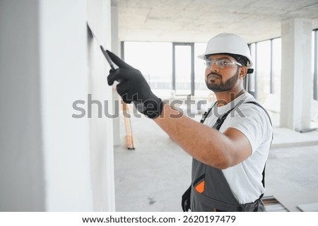 Professional worker plastering wall with putty knife indoors.