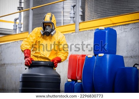 Professional worker in protection suit and gas mask opening barrels with hydrochloric acid inside chemicals production plant.