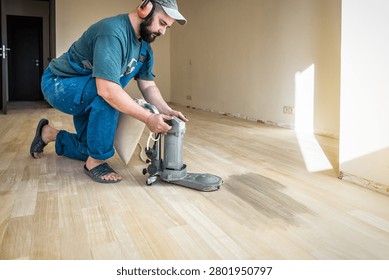 Professional worker in safety muffs using floor edger sander machine on wooden floor. Industrial theme