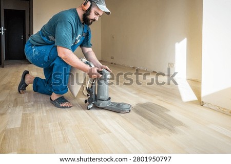 Professional worker in safety muffs using floor edger sander machine on wooden floor. Industrial theme