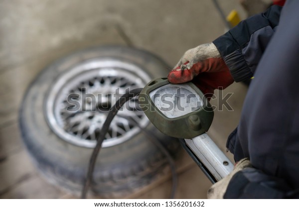A professional worker in a service\
station pumps the pressure of the wheels of a\
car.