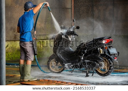 Professional worker using a hose for detailed cleaning. Spraying and washing a motorbike in professional car wash station.