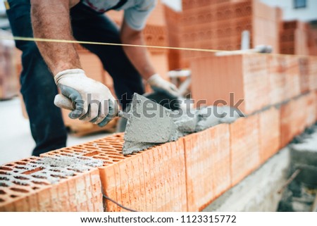 Professional worker using pan knife for building brick walls with cement and mortar