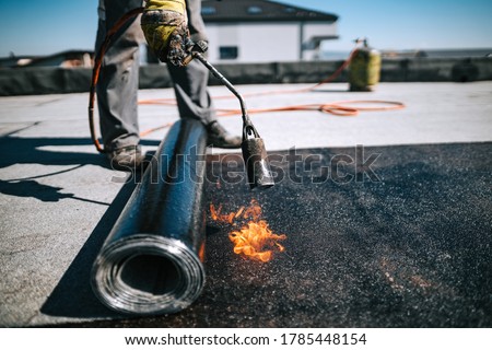 Professional workers insulating rooftop with bitumen membrane. Waterproofing details at construction site. Bituminous membrane waterproofing system details and installation on flat rooftop.
