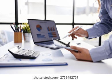 A professional working on a tablet while analyzing data charts on a laptop in a sleek office environment, showcasing teamwork and modern technology.