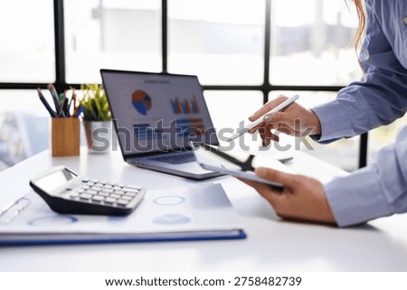 A professional working on a tablet while analyzing data charts on a laptop in a sleek office environment, showcasing teamwork and modern technology.
