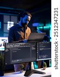 IT professional working from RGB lit home using laptop, testing and deploying programs and systems. Software engineer checking code displayed on computer monitors, standing in apartment