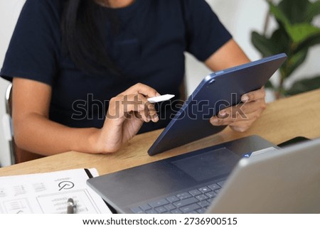Professional working with tablet and stylus while using laptop at modern workspace desk. Concept of digital design, business workflow, UX UI planning, remote work, productivity, technology, and creative process.