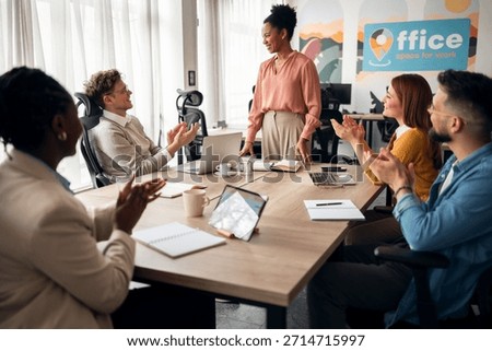 A professional workplace setting featuring diverse coworkers applauding during a team meeting, symbolizing teamwork and success.