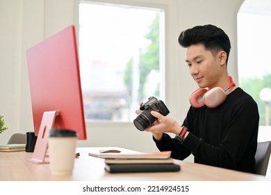 Professional young Asian male photographer holding, looking, checking or adjusting a camera before shooting at his desk. - Powered by Shutterstock