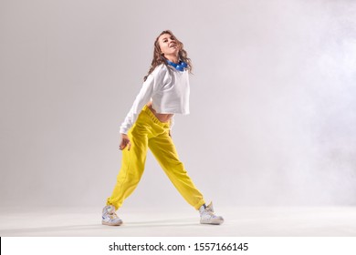 Professional Young Female Dancer In Motion, Looking At Camera With Cheerful Expression, Stands On White Floor With Happily Opened Mouth, Focused On Training , Isolated On White Background