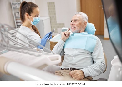 Professional Young Female Dentist Holding A Tablet And Looking At A Senior Man In A Dental Chair During A Consultation