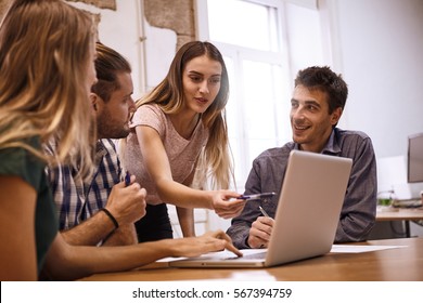 Professional Young Female Presenter Pointing To And Explaining Something On The Laptop Pc With Enthusiasm To The Rest Of The Team In A Meeting