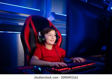 Professional young gamer boy with headphones sitting in comfortable chair and playing computer video game.