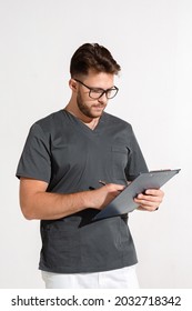 Professional Young Male Physician Practitioner In Glasses Writing Doctor Report, Prescribe Treatment On White Background