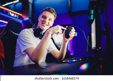 Professional young man player in online video game cybersportsman advertises headphones, keyboard and mouse for computer, blurred background.