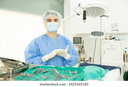 Professional young veterinarian in sterile coat, cap, mask and gloves preparing to conduct surgical operation at veterinary clinic, standing by operating table, confidently looking into camera.. - Powered by Shutterstock