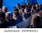 Professionally dressed audience members at a corporate event are focused on a presentation, illustrating engagement and professional development in a business setting.